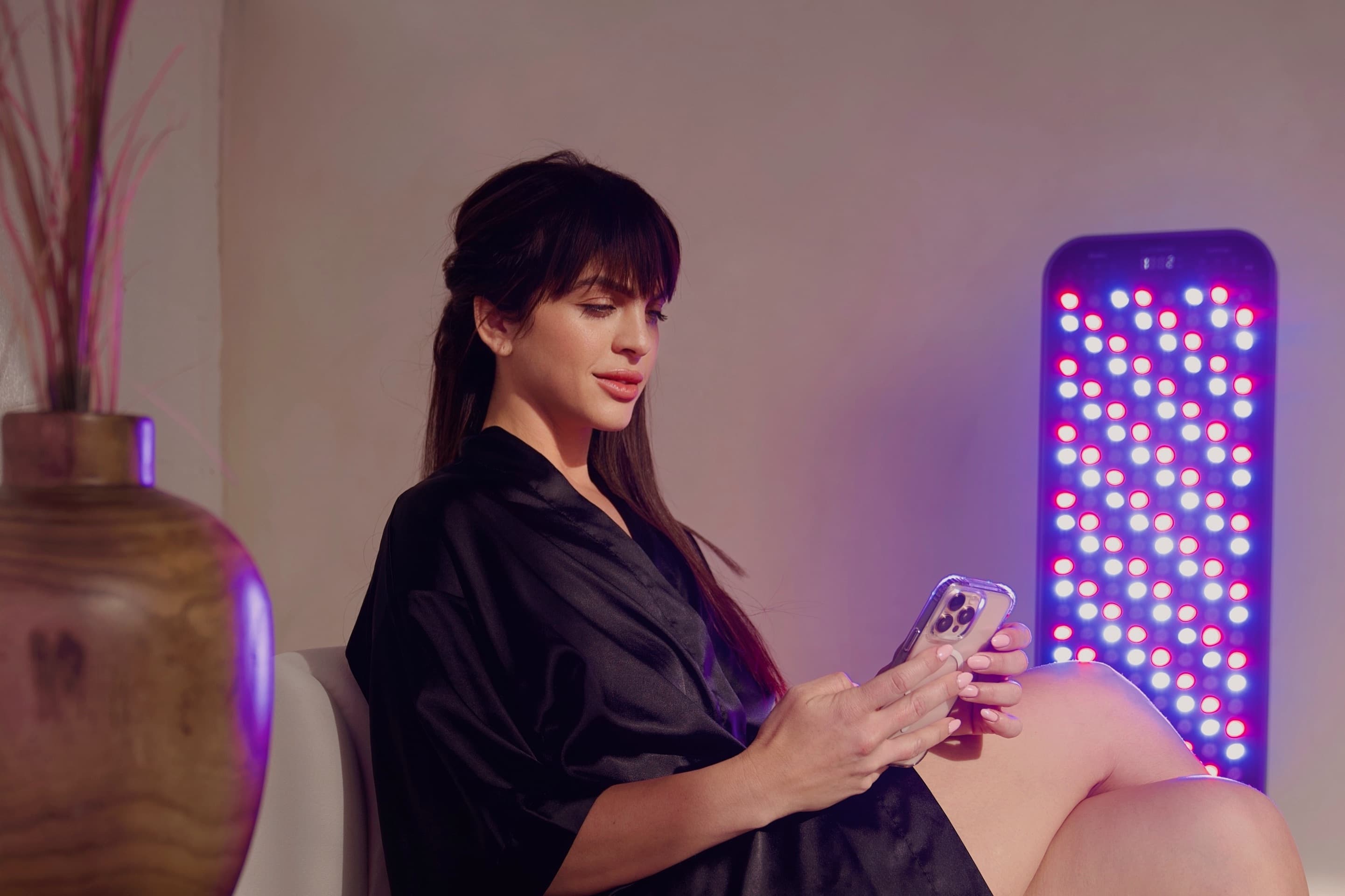 Client in a black robe resting beside a glowing red-light therapy panel