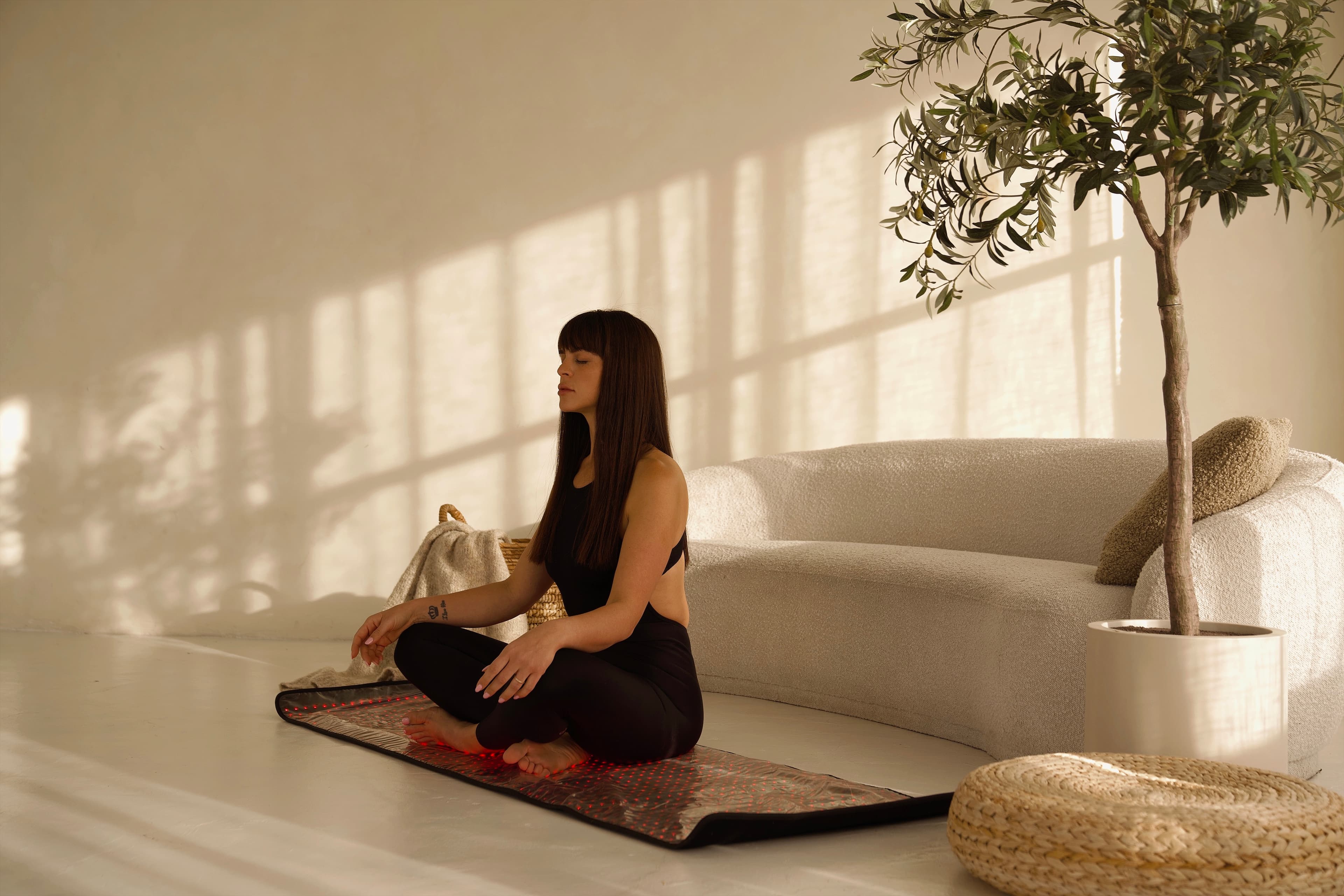 Woman meditating on a mat beside a curved cream sofa in soft shadow-play light